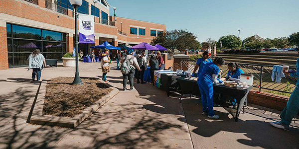 Wide shot of tables set up outside the MGA Student Life Center. Students can be seen receiving information from different booths.